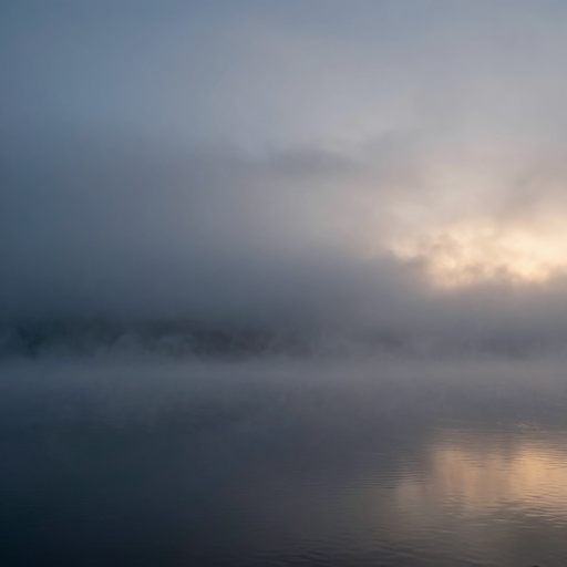 A low-lying, dense fog receding over a vast, still body of water at dawn, symbolizing the lessening of emotional pressure.